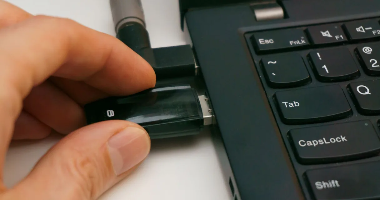 Mão inserindo um pen drive na porta USB de um notebook preto